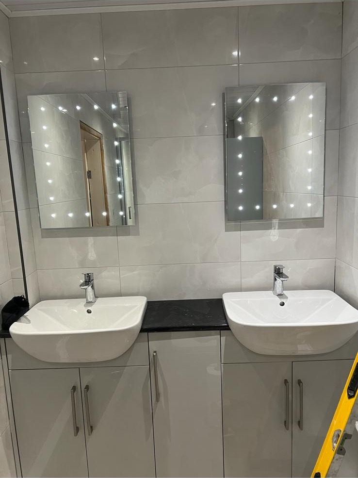 Twin basin vanity run with illuminated mirrors and black worktop in a serviced bathroom